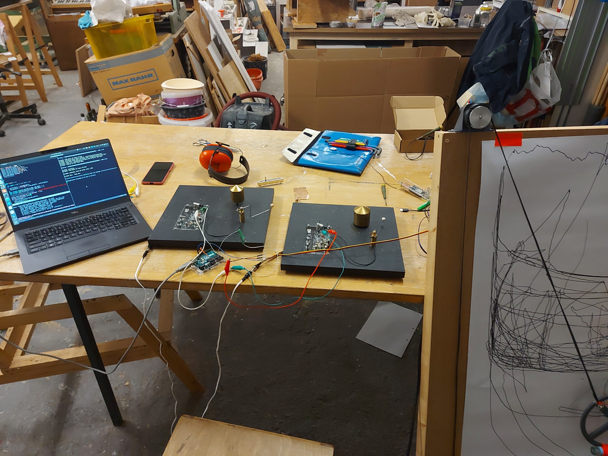 Image shows a computer on a table with two motor and bell holders and a drawing machine.